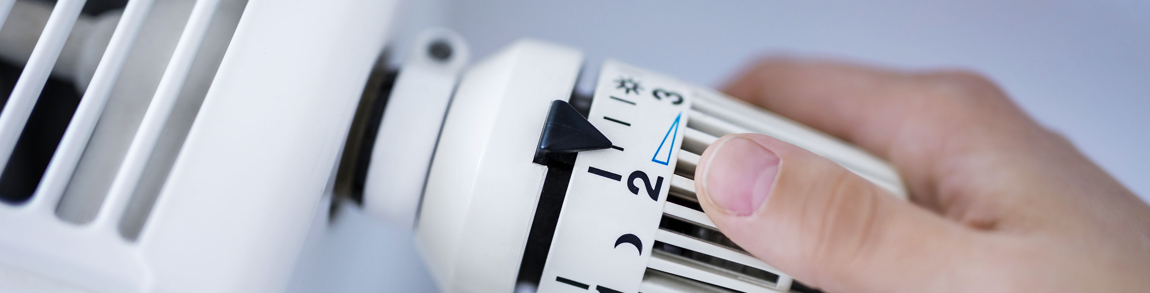 Das Bild zeigt eine Hand, die an einem Heizungsthermostat dreht